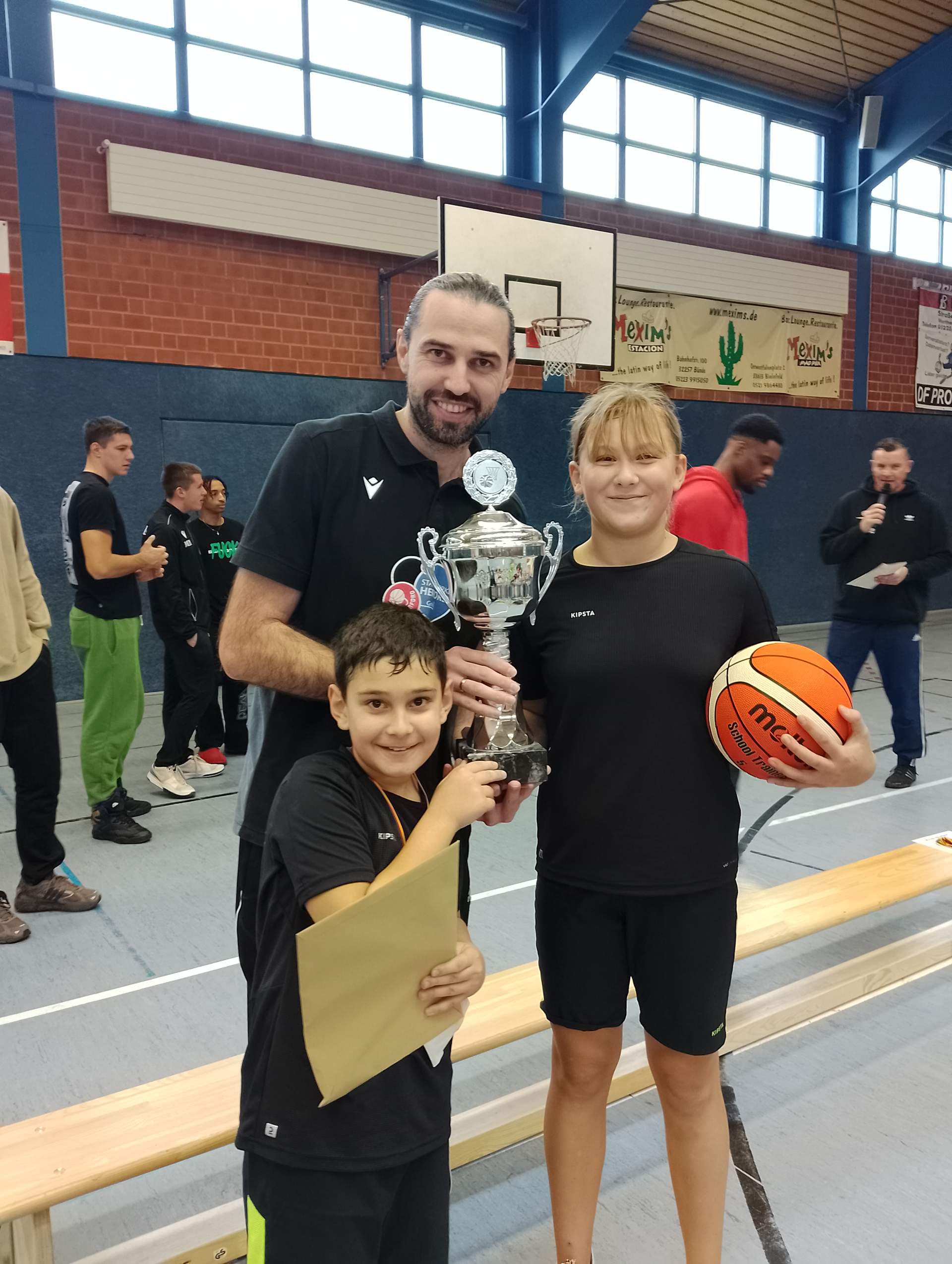 Trainer mit Pokal in der Hand mit 2 Kindern