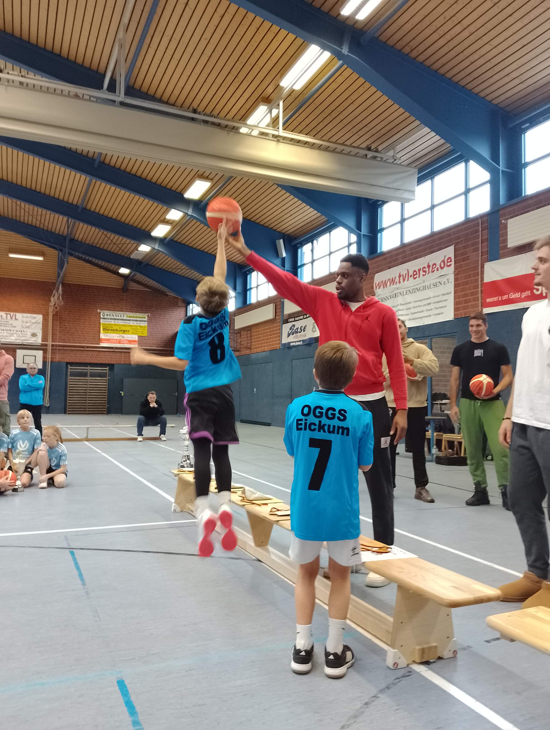 Spieler hält Basketball hoch und Kinde springt um den Ball zu holen